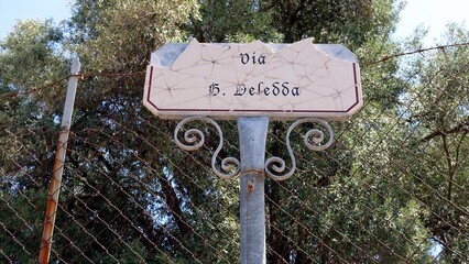 A ruined marble road sign with the name of a street dedicated to a Nobel Prize for Literature.
