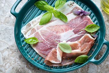 Slices of italian prosciutto with fresh basil leaves on a green serving tray, middle close-up,...