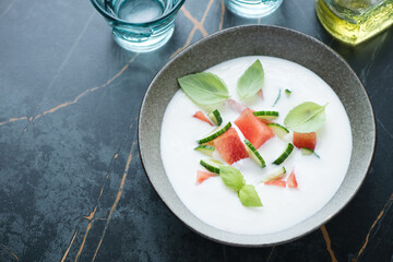 Bowl of cold soup with buttermilk, watermelon and cucumber, high angle view on a dark-olive marble background with space