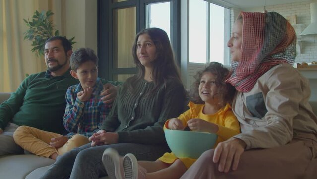 Portrait Of Cheerful Relaxed Beautiful Arab Family With Many Children Spending Weekend Together, Friendly Chatting And Sharing While Watching Entertaining Program On Tv In Living Room.