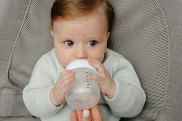 A charming blue-eyed baby of 5 months lies in bed and drinks milk from a bottle	