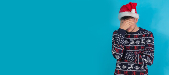 isolated young man with christmas sweater and santa claus hat sad or overwhelmed expression