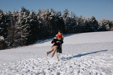 Mother circles her daughter in winter in a field near a snow-covered forest of fir trees.