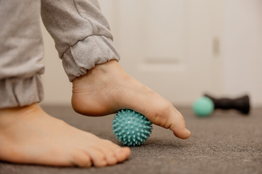 Woman doing flatfoot correction gymnastic exercise using massage ball. Myofascial relaxation of foot muscles. Hallux valgus. Pain. Identification of flat feet. Self care practices at home, healthcare.