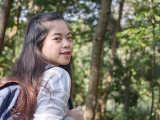 Happy young Asian woman with backpack walking on path in summer forest.