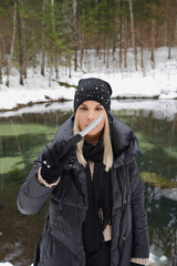 A beautiful girl with a knife in her hand stands near a forest lake in winter.