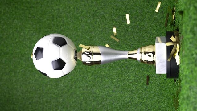 Soccer champion trophy revolves around itself with falling golden confetti. Vertical video 4K