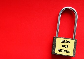 Lock pad on red copy space background with stick note written UNLOCK YOUR POTENTIAL, concept of ...
