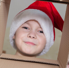 Little Christmas girl in a Santa hat looks into a gift box. Child is happy with a New Year's gift. The background is defocused light. The concept of Christmas and New Year 2022. High quality photo