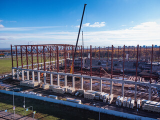 Aerial view of the sports complex under construction. Construction cranes lift the beams of the metal frame of the building onto a concrete base.