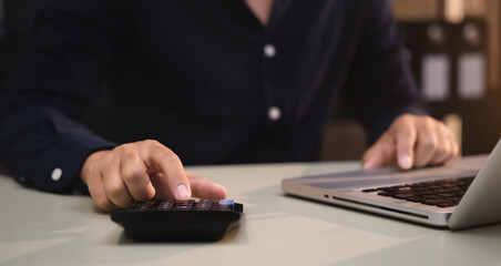 Businessman working with laptop and using a calculator to calculate the tax of static in office. Finance accounting concept.