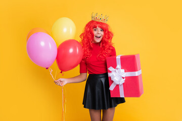 surprised kid in crown with present box and party balloon on yellow background