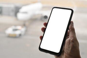 Close-up of a traveler passenger's hand holding a smartphone with a blank white screen on the background of an airplane, selective focus. Mobile phone mockup and airport