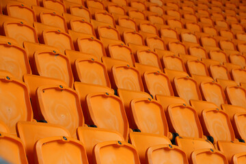 rows of vacant orange fold down seats at a sports stadium