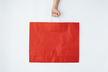 Hand holding red craft shopping bag with sign SALE. Minimal Black Friday shopping, sale, promotion concept with blank copy space mockup