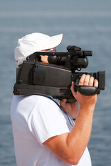 Cameraman holding the huge cam in the right hand while recording a summer event on the river