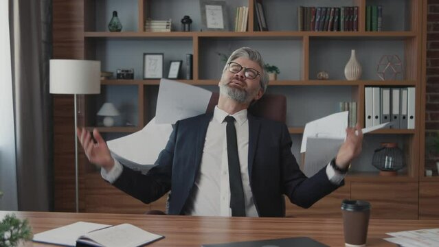 Attractive businessman with glasses sitting holds documents and throws up papers at work place. Relax. Office. Optimistic. Close up