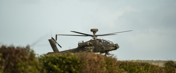 close-up head-on front profile view of a British army Boeing Apache Attack helicopter (AH-64E ZM707 ArmyAir606) hovering low behind hedge cover © Martin