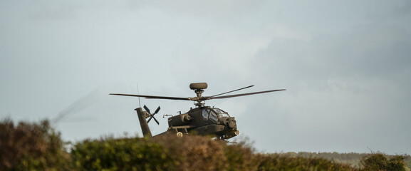 Fototapeta premium close-up front quarter profile view of a British army Boeing Apache Attack helicopter (AH-64E ZM707 ArmyAir606) hovering low behind hedge cover