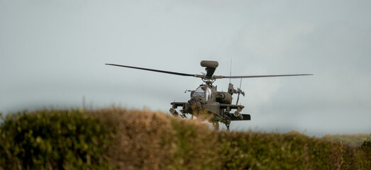 close-up head-on front profile view of a British army Boeing Apache Attack helicopter (AH-64E ZM707 ArmyAir606) hovering low behind hedge cover