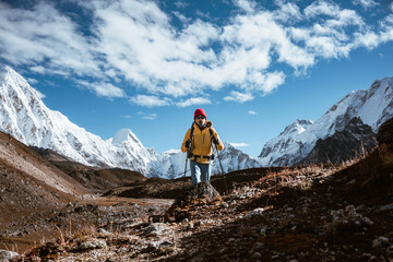 Young tourist walk along high altitude track among snowy and cloudy mountains. Man expeditor with travel backpack going across rocky way