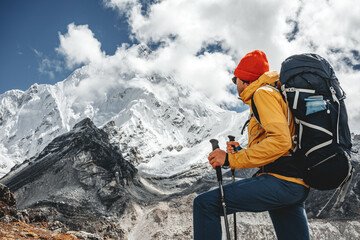 Young tourist walk along high altitude track among snowy and cloudy mountains. Man expeditor with...