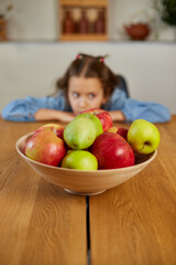 Fototapeta premium Little sad girl look on bowl with fruits in the kitchen at home