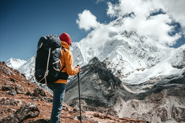 Professional expeditor with trekking sticks and traveling backpack going by mountains tack. Solo tourist hiking across high snowy mountain