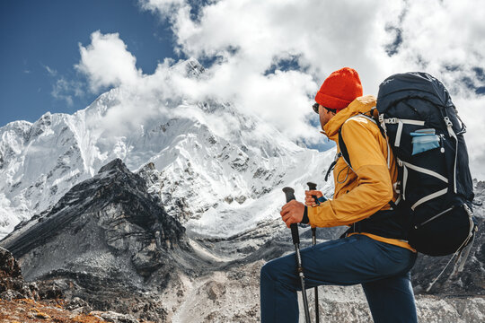Young tourist walk along high altitude track among snowy and cloudy mountains. Man expeditor with travel backpack going across rocky way