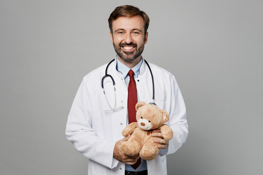 Male pediatrician doctor cheerful man wears white medical gown suit work in hospital hold teddy bear loook camera isolated on plain grey color background studio portrait. Healthcare medicine concept.