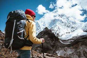 Solo expeditor with travel backpack stand in front of snowy and cloudy mountains. Portrait of man traveler among high altitude mountain