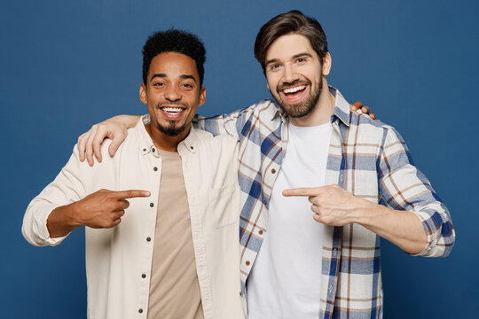 Young two friends fun cool men wear white casual shirts together looking camera put hand on shoulder point finger on each other isolated plain dark royal navy blue background People lifestyle concept