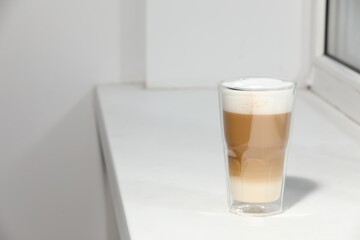 Glass with latte on white window sill. Space for text