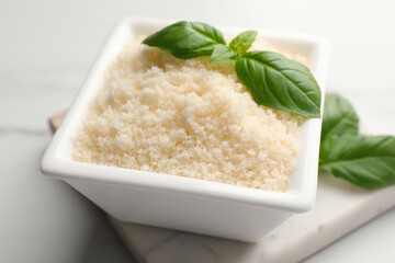 Square bowl with grated parmesan cheese and basil on white table, closeup