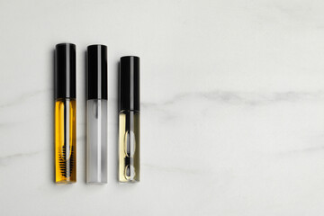 Tube of different eyelash oils on white marble table, flat lay. Space for text