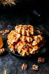 Belgian waffles with honey and nuts on a dark background