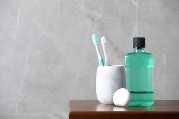 Bottle of mouthwash, toothbrushes and dental floss on wooden table, space for text