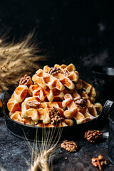 Belgian waffles with honey and nuts on a dark background