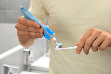 Man applying toothpaste on brush in bathroom, closeup - Powered by Adobe