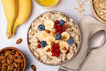 Oatmeal served with berries, almonds and banana slices on white tiled table, flat lay