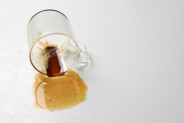 Overturned cup and spilled coffee on light table. Space for text