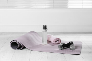 Exercise mat, dumbbells, towel and bottle of water on light wooden floor indoors - Powered by Adobe