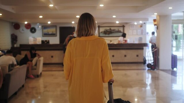 Attractive woman arriving at hotel reception lobby, vacation trip, check-in with luggage using payment device. Travel and reception desk concept