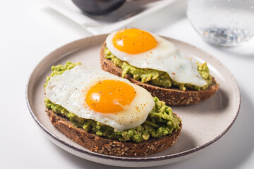 Avocado egg sandwich with a glass of water. Healthy light breakfast concept. Whole grain toasts with mashed avocado and fried eggs