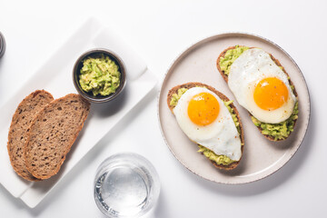 Avocado egg sandwich with a glass of water. Healthy light breakfast concept. Whole grain toasts with mashed avocado and fried eggs