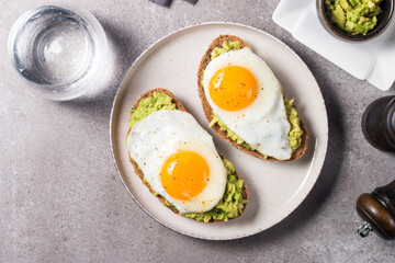 Avocado egg sandwich with a glass of water. Healthy light breakfast concept. Whole grain toasts with mashed avocado and fried eggs