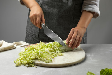Woman cutting fresh Chinese cabbage at light grey table, closeup