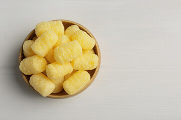 Bowl of delicious crispy corn sticks on white wooden table, top view. Space for text