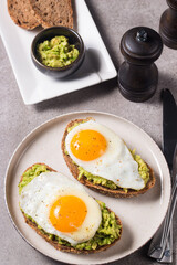 Avocado egg sandwich with a glass of water. Healthy light breakfast concept. Whole grain toasts with mashed avocado and fried eggs