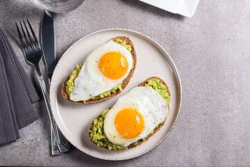 Avocado egg sandwich with a glass of water. Healthy light breakfast concept. Whole grain toasts with mashed avocado and fried eggs